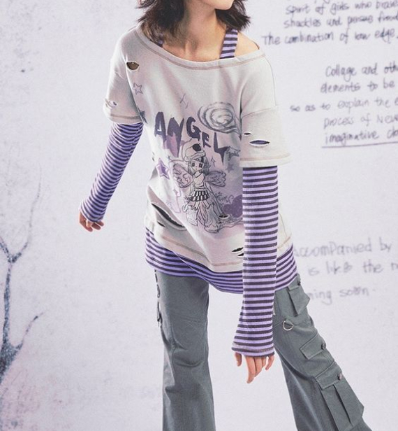 A person models a layered outfit featuring a distressed graphic t-shirt over a purple and white striped long-sleeve top, paired with gray cargo pants with pleated details.